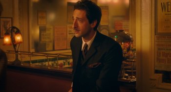 Movie still from “Midnight in Paris” (2011), directed by Woody Allen – A man wearing a suit and tie sitting at a table; Medium shot, Over the shoulder angle
