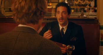 Movie still from “Midnight in Paris” (2011), directed by Woody Allen – A man sitting at a table talking to another man in a suit; Medium shot, Over the shoulder angle