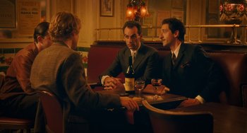 Movie still from “Midnight in Paris” (2011), directed by Woody Allen – A group of men sitting at a table with a bottle of wine; Medium shot, Over the shoulder angle