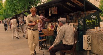 Movie still from “Midnight in Paris” (2011), directed by Woody Allen – A man standing next to a man sitting next to another man; Wide shot, Over the shoulder angle