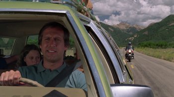 Movie still from “Vacation” (1983), directed by Harold Ramis – A man driving a car on the side of the road; Medium shot, Low angle