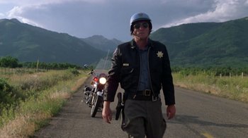 Movie still from “Vacation” (1983), directed by Harold Ramis – A police officer walking down a road with a motorcycle behind him; Medium shot, Low angle