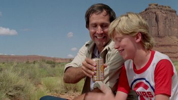 Movie still from “Vacation” (1983), directed by Harold Ramis – A man and a boy sitting on the ground with a can of soda in front of them; Medium shot, Over the shoulder angle