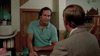 Movie still from “Vacation” (1983), directed by Harold Ramis – A man sitting at a table talking to another man in a suit; Medium shot, Over the shoulder angle
