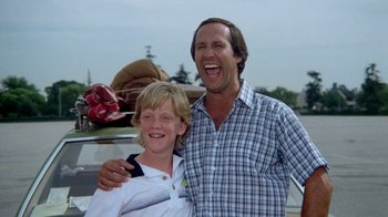 Movie still from “Vacation” (1983), directed by Harold Ramis – A man and a boy standing next to each other in front of a car; Medium shot, Low angle
