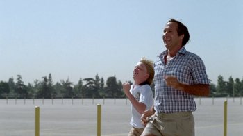 Movie still from “Vacation” (1983), directed by Harold Ramis – A man and a boy are running in a parking lot; Medium shot, Low angle