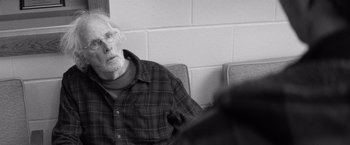 Movie still from “Nebraska” (2013), directed by Alexander Payne – An older man sitting on a chair in front of a brick wall; Close Up shot, Over the shoulder angle