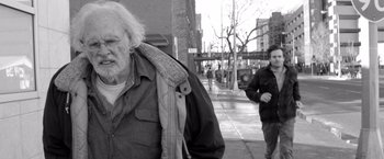 Movie still from “Nebraska” (2013), directed by Alexander Payne – An older man walking down a sidewalk in the rain; Medium shot, Over the shoulder angle