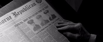 Movie still from “Nebraska” (2013), directed by Alexander Payne – An older person reading a newspaper with a picture of two men in uniform; Extreme Close Up shot, High angle