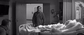 Movie still from “Nebraska” (2013), directed by Alexander Payne – A man standing next to a bed in a hospital room; Wide shot, Over the shoulder angle
