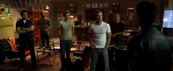 Movie still from “Need for Speed” (2014), directed by Scott Waugh – A group of people standing in a room; Wide shot, Low angle