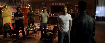 Movie still from “Need for Speed” (2014), directed by Scott Waugh – A group of young men standing in a living room; Wide shot, Over the shoulder angle