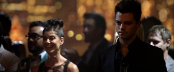 Movie still from “Need for Speed” (2014), directed by Scott Waugh – A man and a woman standing next to each other in front of lights; Close Up shot, Over the shoulder angle