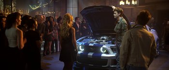 Movie still from “Need for Speed” (2014), directed by Scott Waugh – A group of people standing next to an open hood of a sports car; Wide shot, Over the shoulder angle