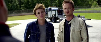 Movie still from “Need for Speed” (2014), directed by Scott Waugh – Two men standing next to each other in front of a truck; Medium shot, Low angle