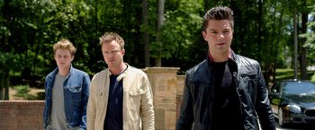 Movie still from “Need for Speed” (2014), directed by Scott Waugh – Two men standing next to each other near a tree; Medium shot, Over the shoulder angle