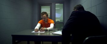 Movie still from “Need for Speed” (2014), directed by Scott Waugh – A man sitting at a table in an orange shirt; Medium shot, Over the shoulder angle