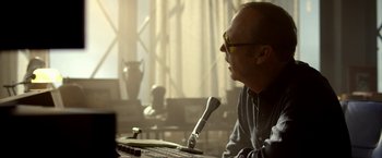 Movie still from “Need for Speed” (2014), directed by Scott Waugh – A man sitting at a table with a microphone; Close Up shot, Over the shoulder angle