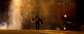 Movie still from “Need for Speed” (2014), directed by Scott Waugh – A man holding a woman on a street with smoke; Wide shot, Low angle