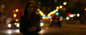 Movie still from “Need for Speed” (2014), directed by Scott Waugh – A woman standing on a street at night with lights in the background; Medium shot, Over the shoulder angle