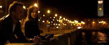 Movie still from “Need for Speed” (2014), directed by Scott Waugh – A woman sitting on top of a railing at night; Medium shot, Over the shoulder angle