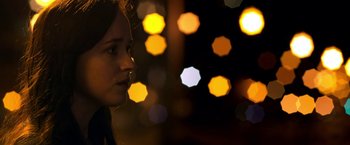 Movie still from “Need for Speed” (2014), directed by Scott Waugh – A woman is standing in front of a bunch of lights; Close Up shot, Over the shoulder angle