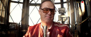 Movie still from “Need for Speed” (2014), directed by Scott Waugh – A person wearing glasses and holding a microphone; Close Up shot, Low angle