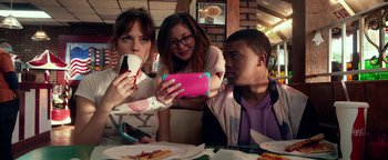 Movie still from “Nerve” (2016), directed by Henry Joost – A group of people sitting at a table looking at a cell phone; Medium shot, Over the shoulder angle