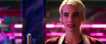 Movie still from “Nerve” (2016), directed by Henry Joost – A young woman smiles brightly at the camera in front of neon lights; Close Up shot, Over the shoulder angle