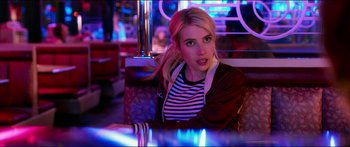 Movie still from “Nerve” (2016), directed by Henry Joost – A woman sitting at a table in front of neon lights; Close Up shot, Over the shoulder angle