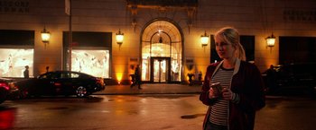 Movie still from “Nerve” (2016), directed by Henry Joost – A woman standing on the sidewalk in front of a building at night; Medium shot, Over the shoulder angle