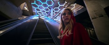 Movie still from “Nerve” (2016), directed by Henry Joost – A woman in a red jacket standing in front of an escalator; Medium shot, Low angle