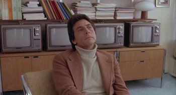 Movie still from “Network” (1976), directed by Sidney Lumet – A man sitting in a chair in front of a bunch of books; Medium shot, Low angle