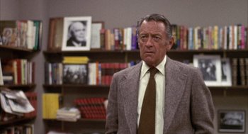 Movie still from “Network” (1976), directed by Sidney Lumet – An older man wearing a suit and tie in front of a book shelf; Medium shot, Over the shoulder angle