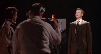 Movie still from “Network” (1976), directed by Sidney Lumet – A man is taking a picture of another man in a brown suit; Medium shot, Low angle