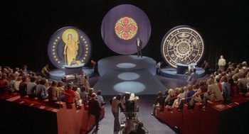 Movie still from “Network” (1976), directed by Sidney Lumet – A group of people sitting in front of a camera; Extreme Wide shot, High angle