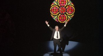 Movie still from “Network” (1976), directed by Sidney Lumet – A man standing in front of a stained - glass window; Wide shot, Low angle