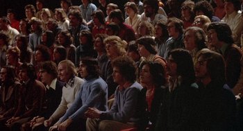 Movie still from “Network” (1976), directed by Sidney Lumet – A group of people sitting in a room watching a show; Wide shot, High angle