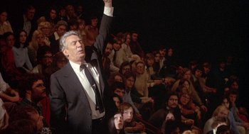Movie still from “Network” (1976), directed by Sidney Lumet – An older man raises his hand in front of an audience; Medium shot, Low angle