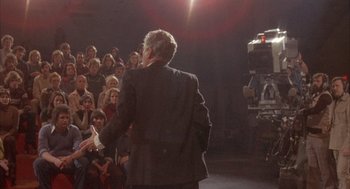 Movie still from “Network” (1976), directed by Sidney Lumet – A man in a suit is giving a speech to a group of people; Wide shot, High angle