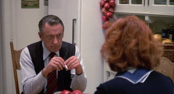 Movie still from “Network” (1976), directed by Sidney Lumet – An older man sitting at a table with a cigarette in his mouth; Medium shot, Over the shoulder angle