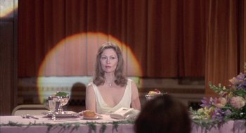 Movie still from “Network” (1976), directed by Sidney Lumet – A woman sitting at a table with a book in front of her; Medium shot, Over the shoulder angle