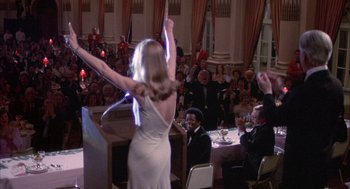 Movie still from “Network” (1976), directed by Sidney Lumet – A woman in a white dress raises her hands in the air; Wide shot, Low angle