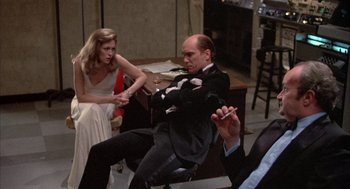 Movie still from “Network” (1976), directed by Sidney Lumet – A man and a woman sitting on a chair in front of another man; Medium shot, Over the shoulder angle
