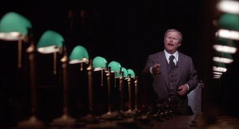 Movie still from “Network” (1976), directed by Sidney Lumet – A man in a suit and tie standing in front of a row of green lamps; Medium shot, Low angle