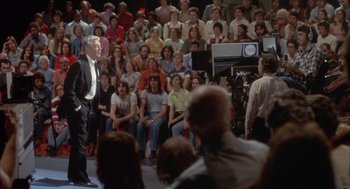 Movie still from “Network” (1976), directed by Sidney Lumet – A group of people sitting in front of an audience; Wide shot, High angle