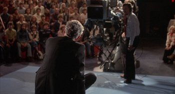 Movie still from “Network” (1976), directed by Sidney Lumet – A man in a black suit is sitting on the ground; Wide shot, High angle