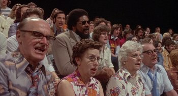 Movie still from “Network” (1976), directed by Sidney Lumet – A group of people sitting in a crowd of people; Medium shot, High angle