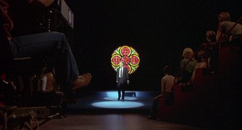 Movie still from “Network” (1976), directed by Sidney Lumet – A man standing in front of a stained - glass window; Extreme Wide shot, Over the shoulder angle