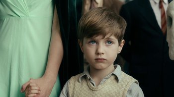 Movie still from “Never Look Away” (2018), directed by Florian Henckel von Donnersmarck – A young boy with blue eyes stares into the camera; Close Up shot, Over the shoulder angle